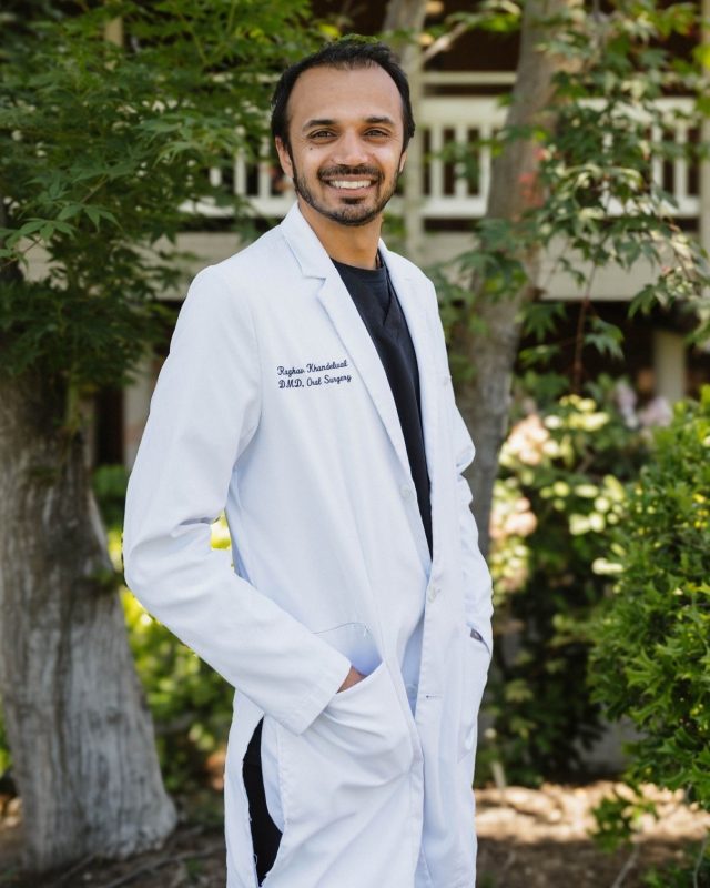 Portrait of Dr. Khandelwal standing outdoors in a white lab coat smiling at the camera